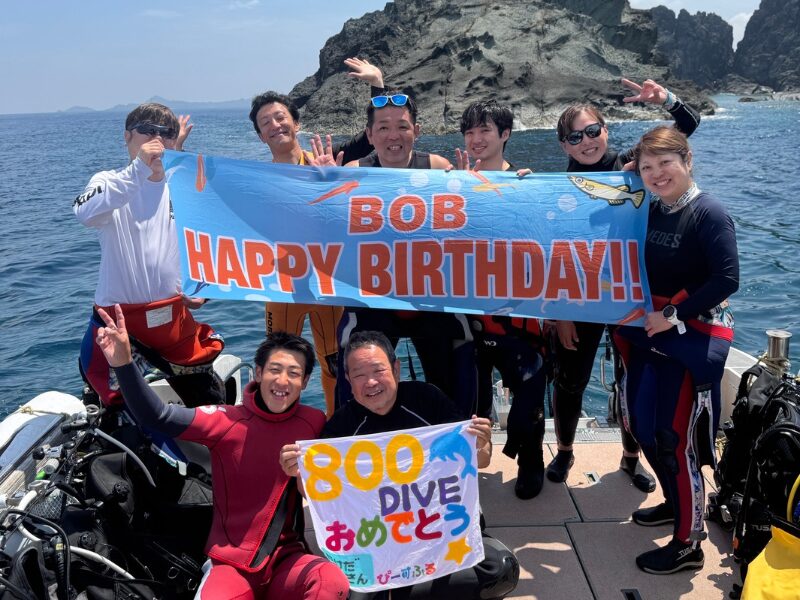 「ボート上でバースデーバナーと800ダイブ達成を掲げるダイバーたち」