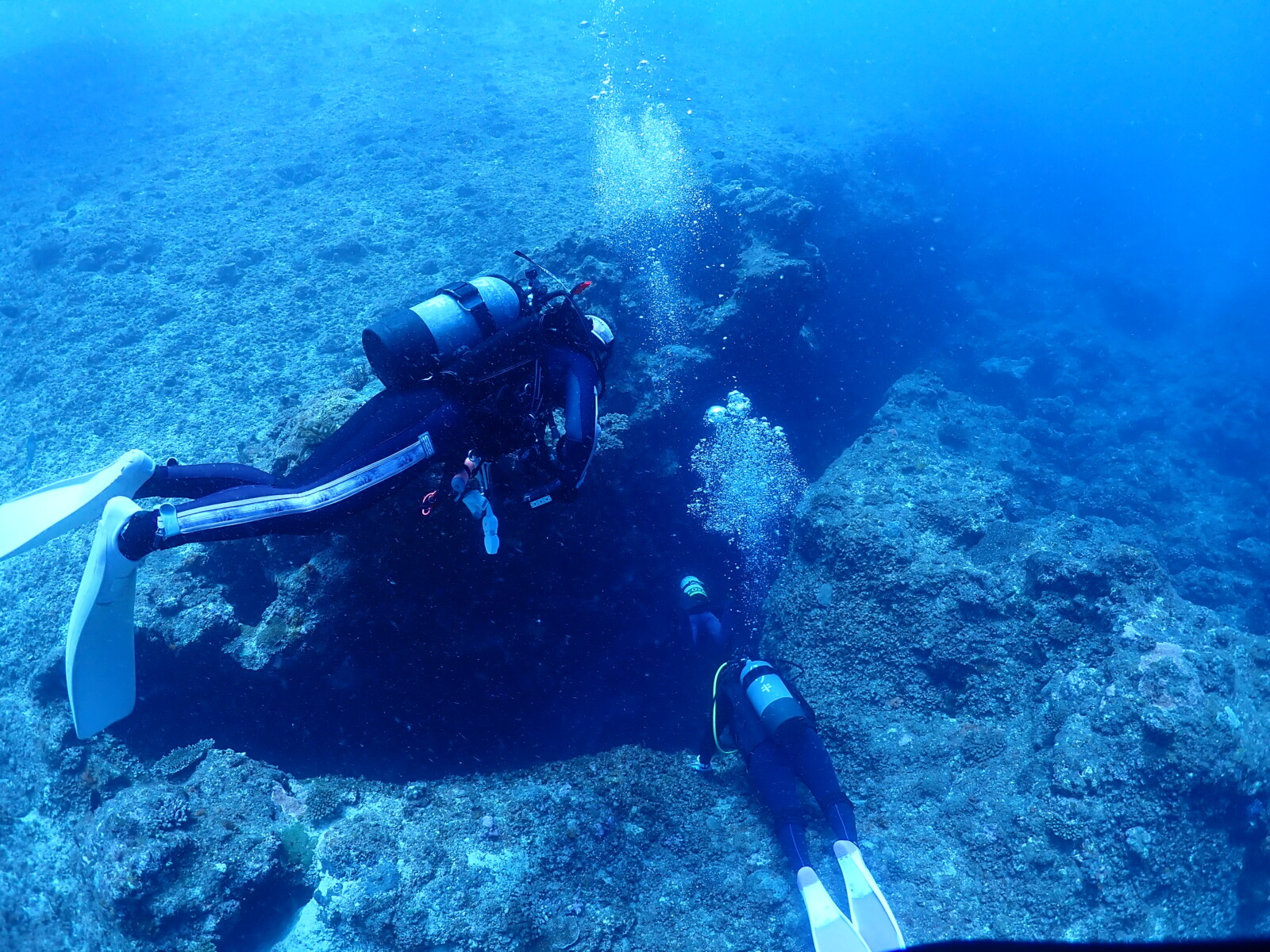 宮古島の海中でダイバーたちが地形ポイントを潜降している様子。青く澄んだ水中に泡が立ち上り、冬の宮古島ダイビングの魅力を表現している。